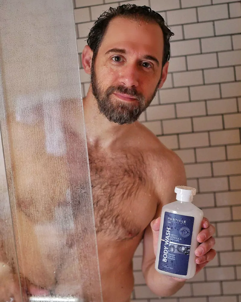 A man in the shower holding a Particle Body Wash bottle.